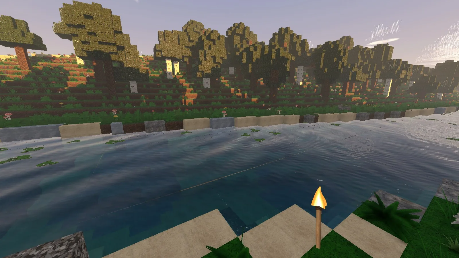 Calm water reflecting a warm evening sky beside a shoreline of trees and sand.